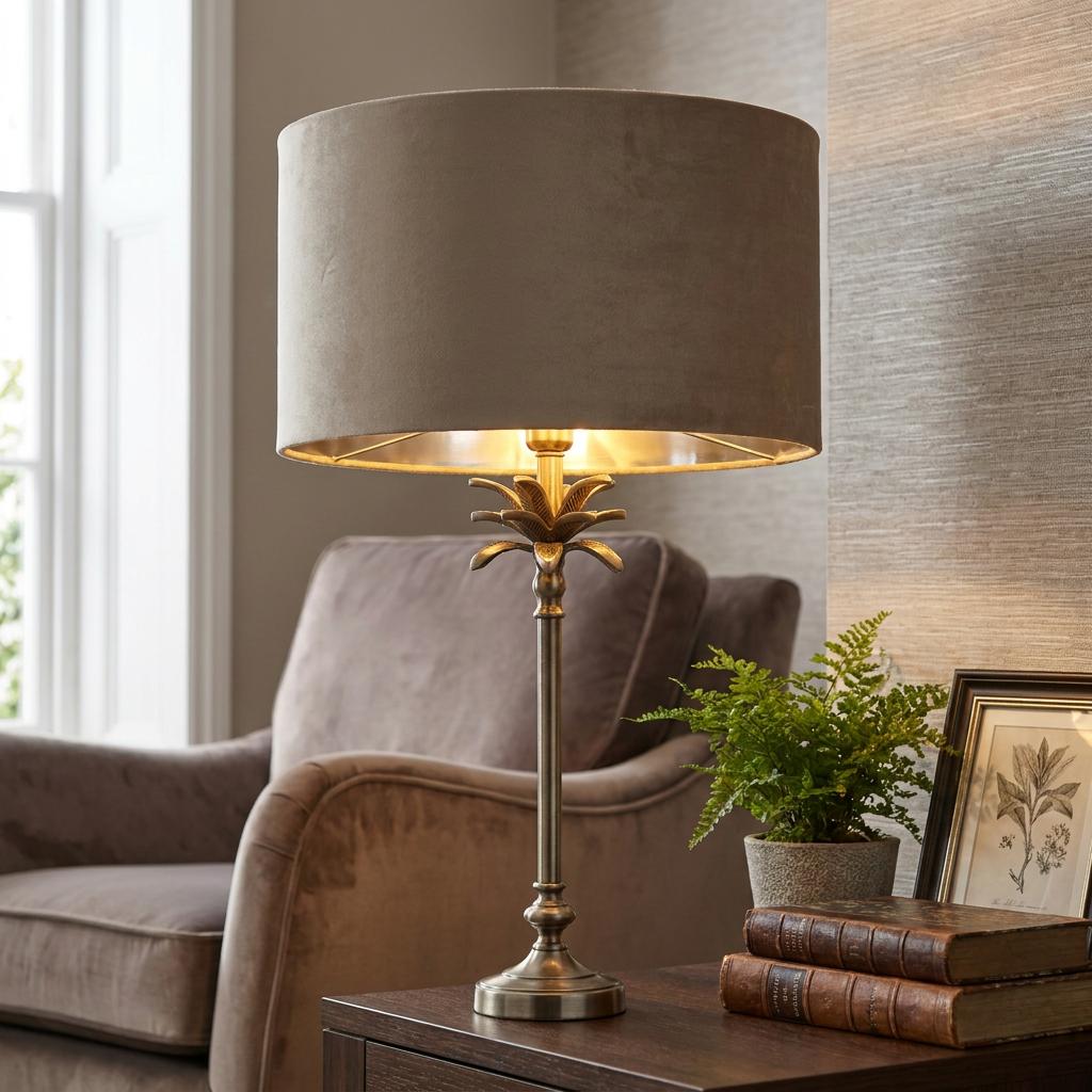 Palm table lamp in antique nickel with a taupe velvet shade on a wooden table in a living room.