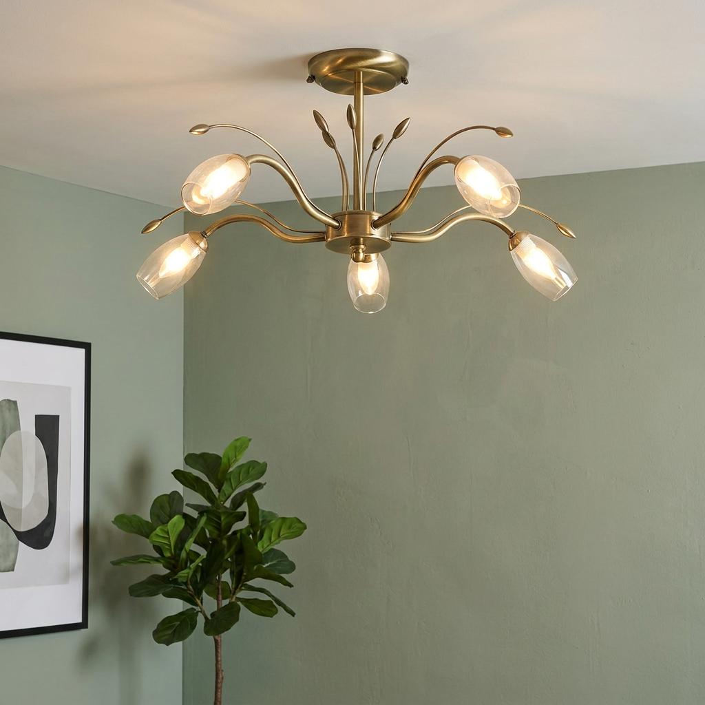 Five-light antique brass semi-flush ceiling light with leaf details and glass shades against a green wall.