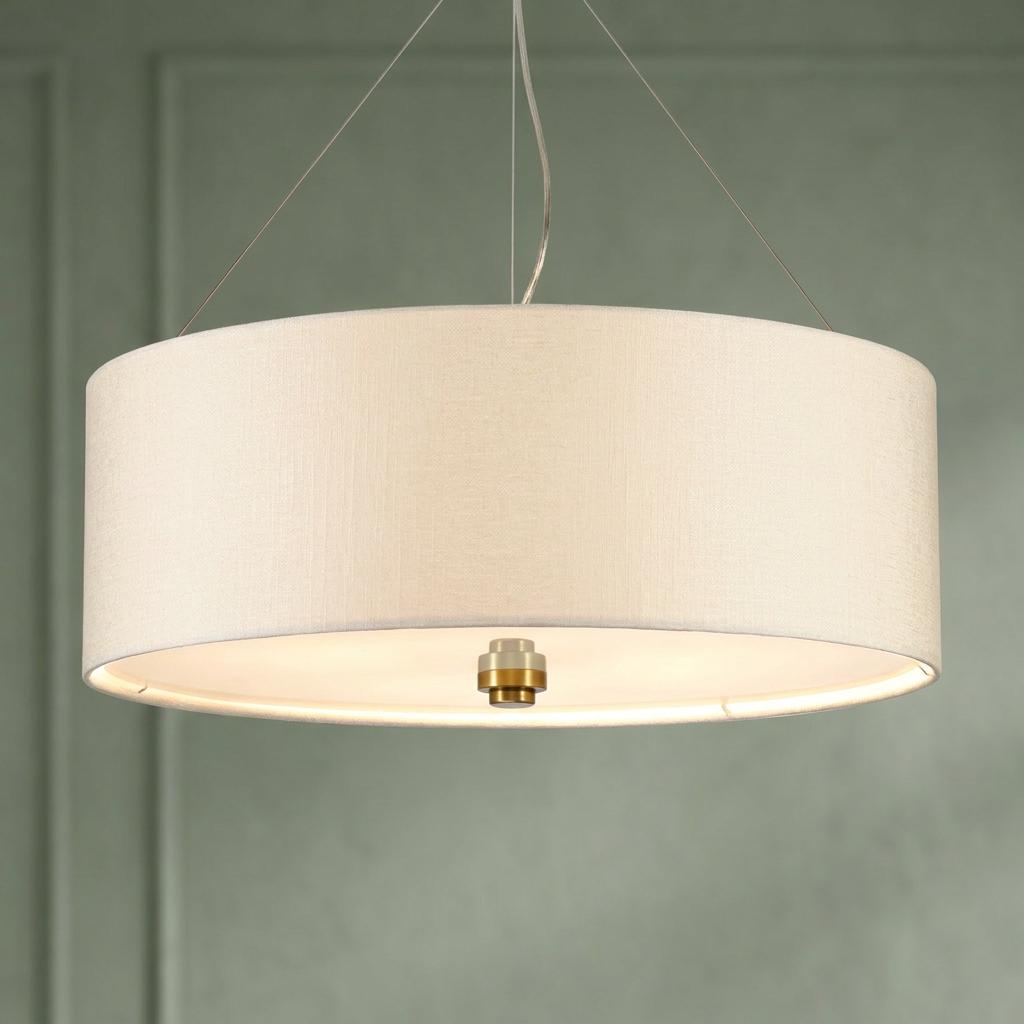 Large cream drum-shaped pendant light with a brass finial suspended against a muted green wall.