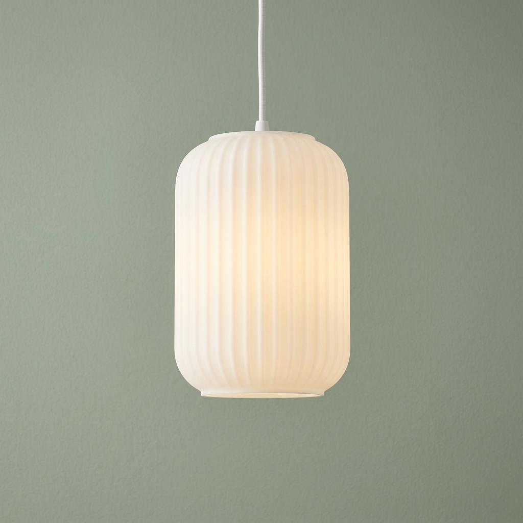 A white frosted glass cylindrical pendant light with a ribbed texture glowing against a sage green wall.