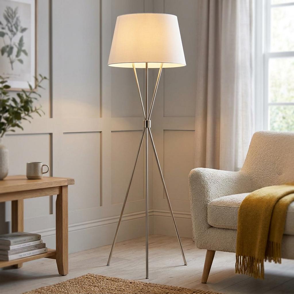 Penny nickel tripod floor lamp with a white drum shade lit up in a cozy living room corner.