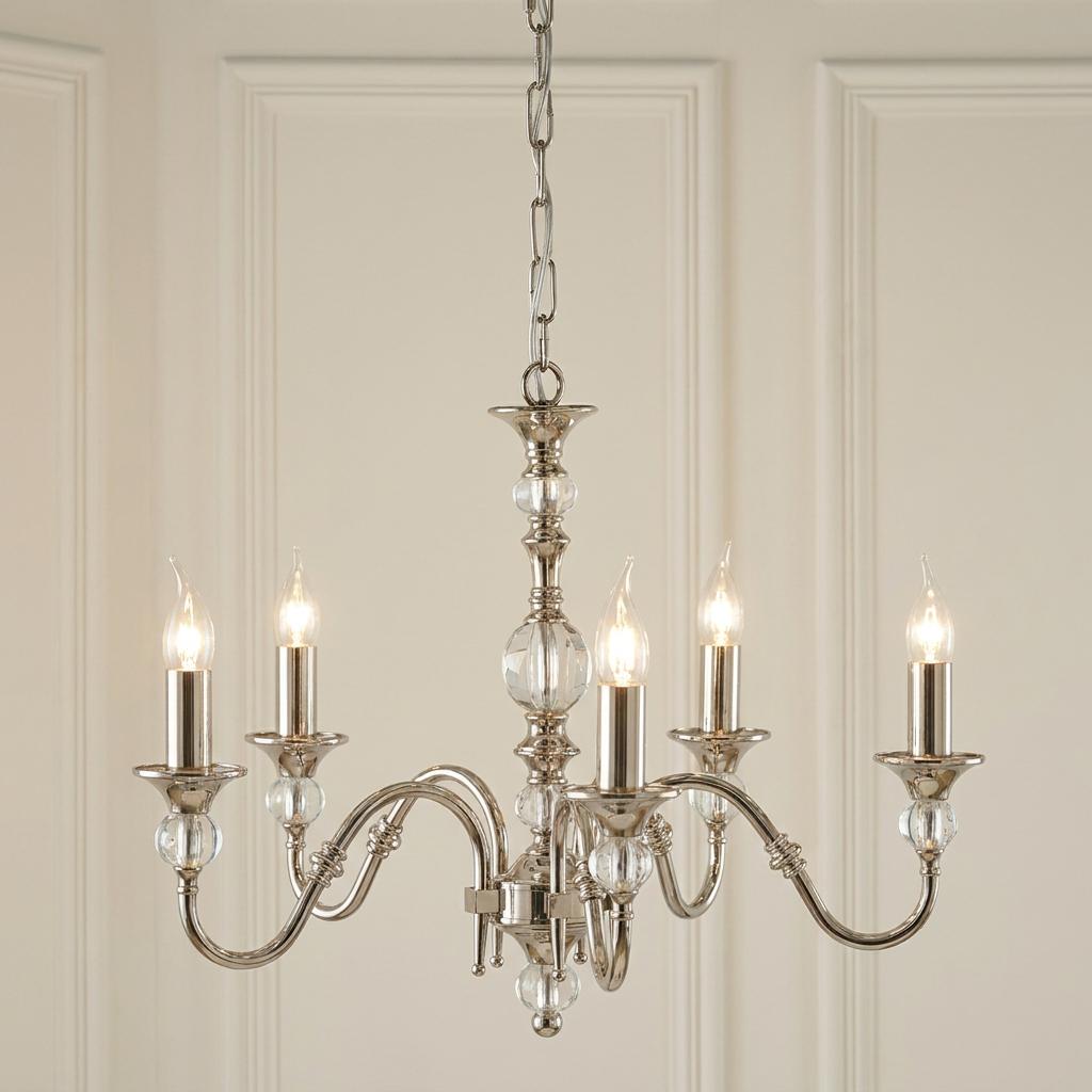Polina 5 light polished nickel chandelier with glass details and candle bulbs against a cream paneled wall.