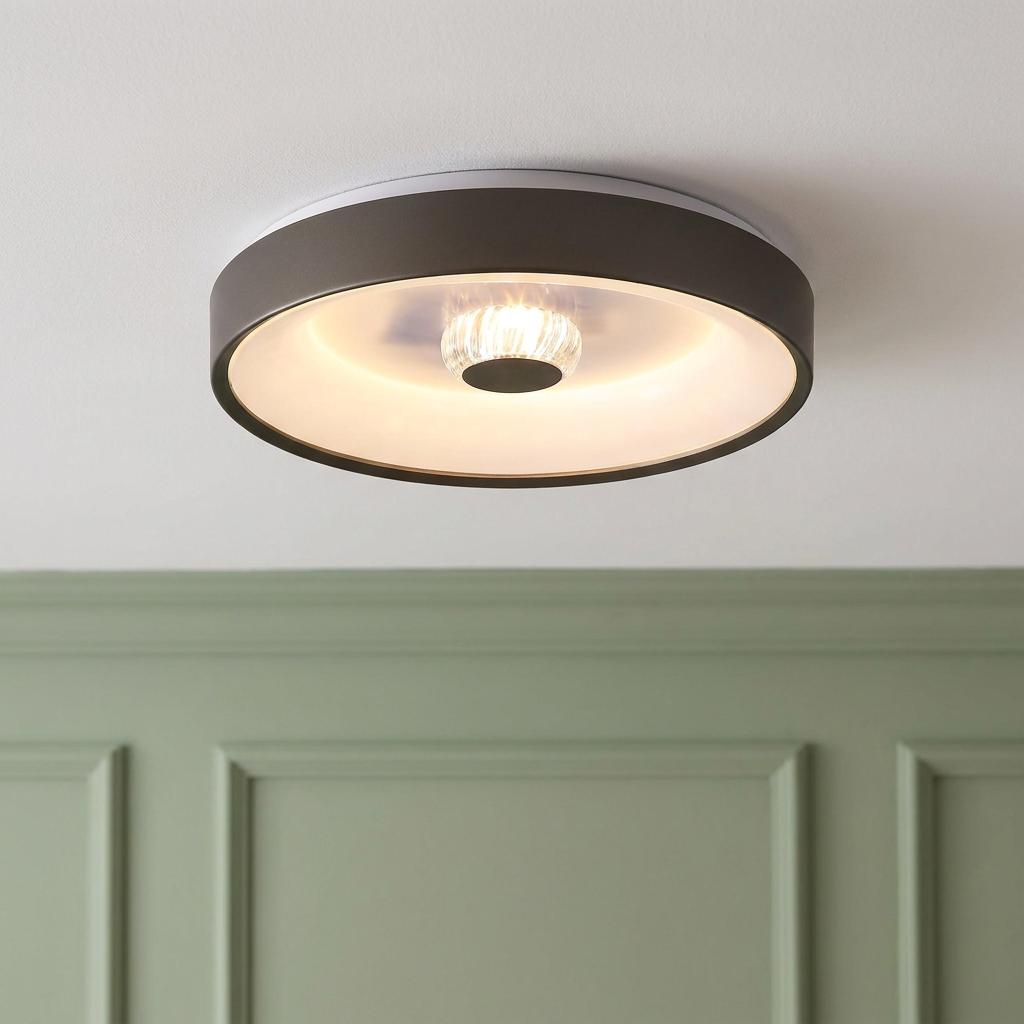 Modern circular latte-colored flush ceiling light with a warm central glow, mounted above green wall paneling.