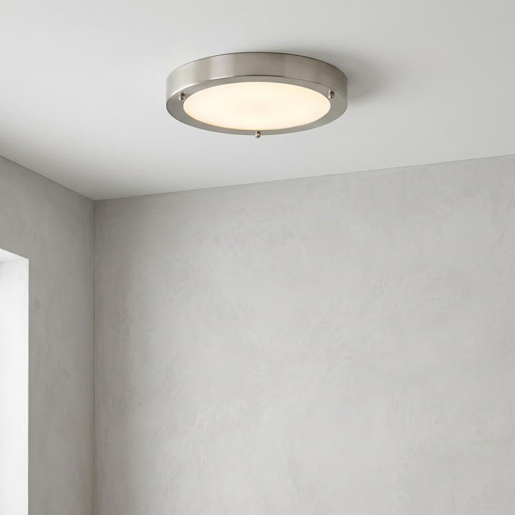 Round brushed nickel flush mount ceiling light with a frosted glass diffuser on a white ceiling.