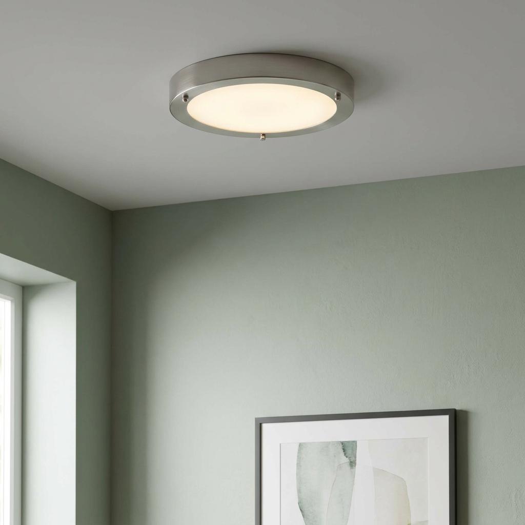 A circular nickel and glass flush LED ceiling light glowing on a white ceiling in a room with sage green walls.