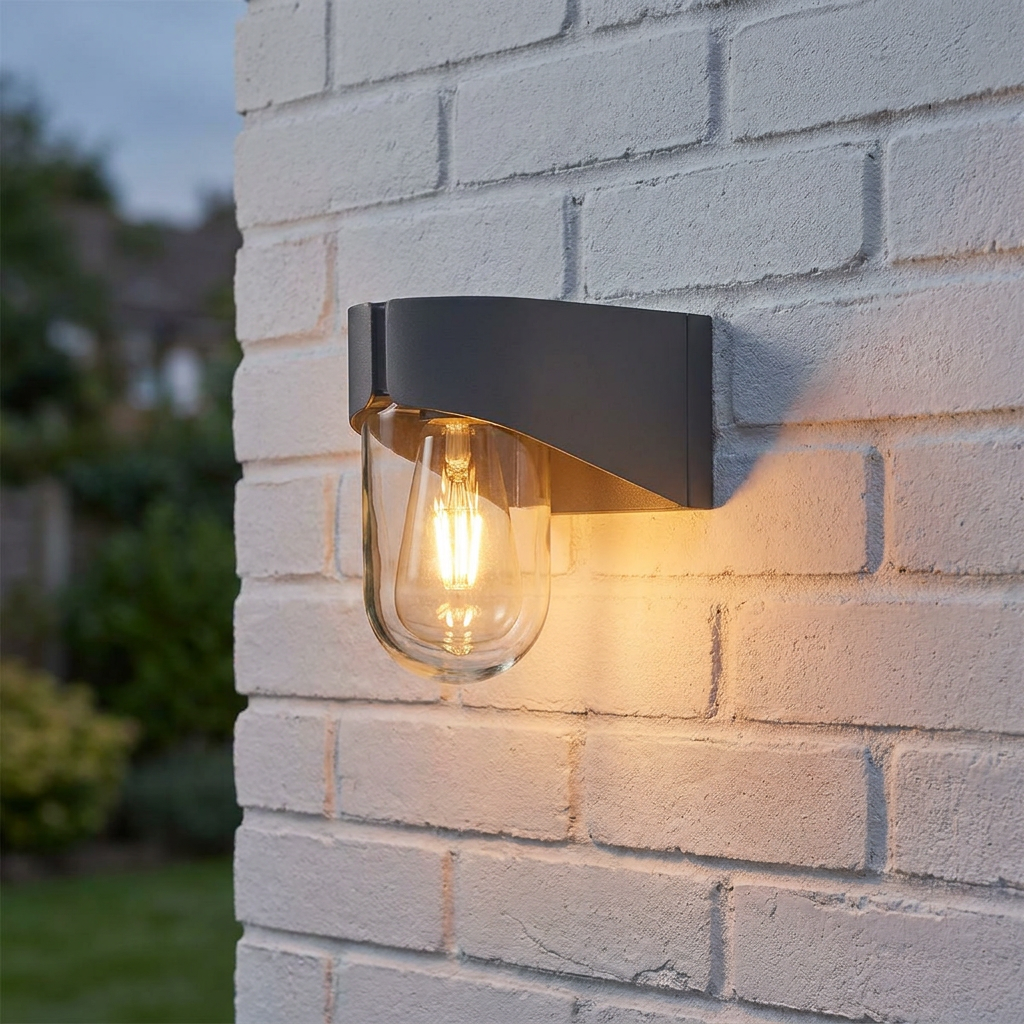 Porto Grey Outdoor Wall Lantern with a warm glowing filament bulb mounted on a white brick wall at dusk.