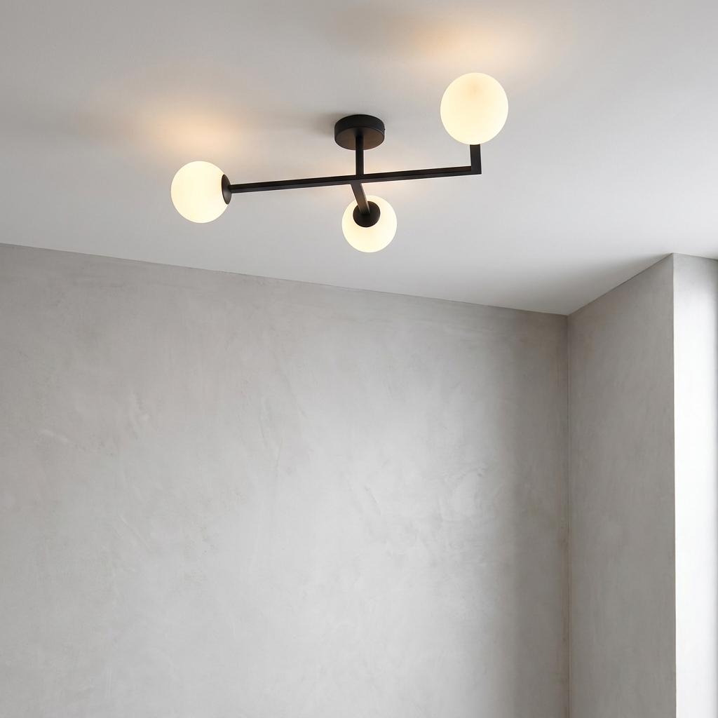 Modern black ceiling light with three white globe shades on a white ceiling against grey walls.