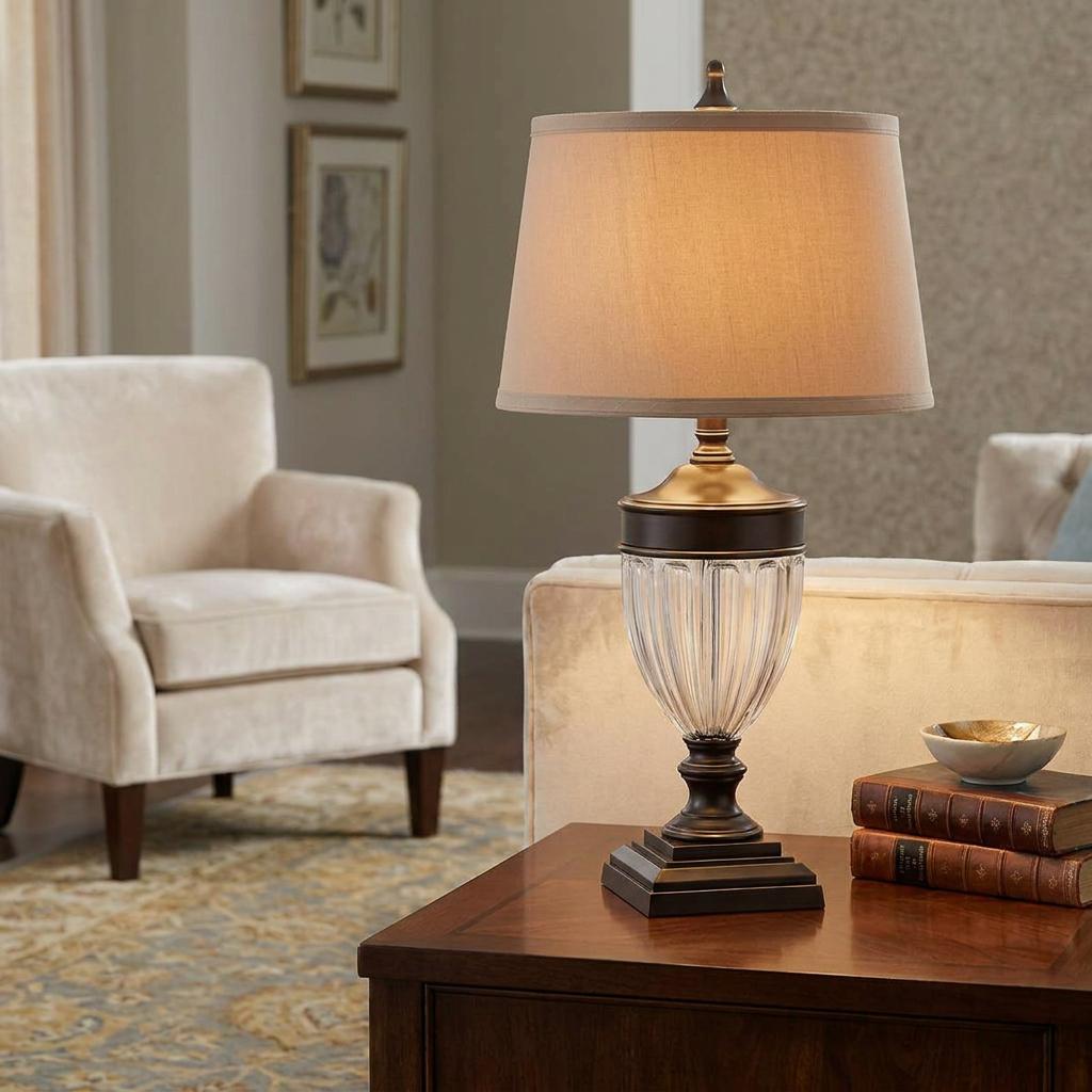 Bronze table lamp with a ribbed glass base and beige shade on a wooden side table in a cozy living room.