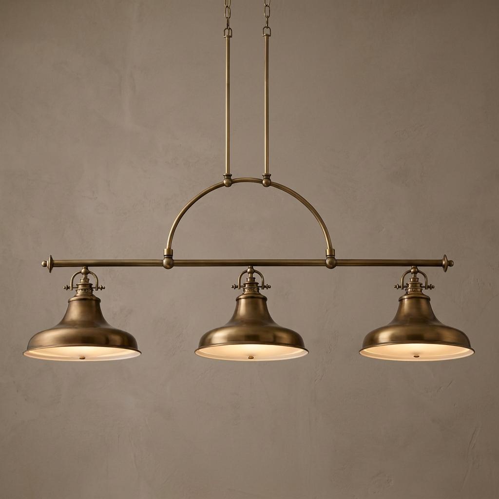 Industrial weathered brass three-light island chandelier with bell shades hanging against a beige textured wall.