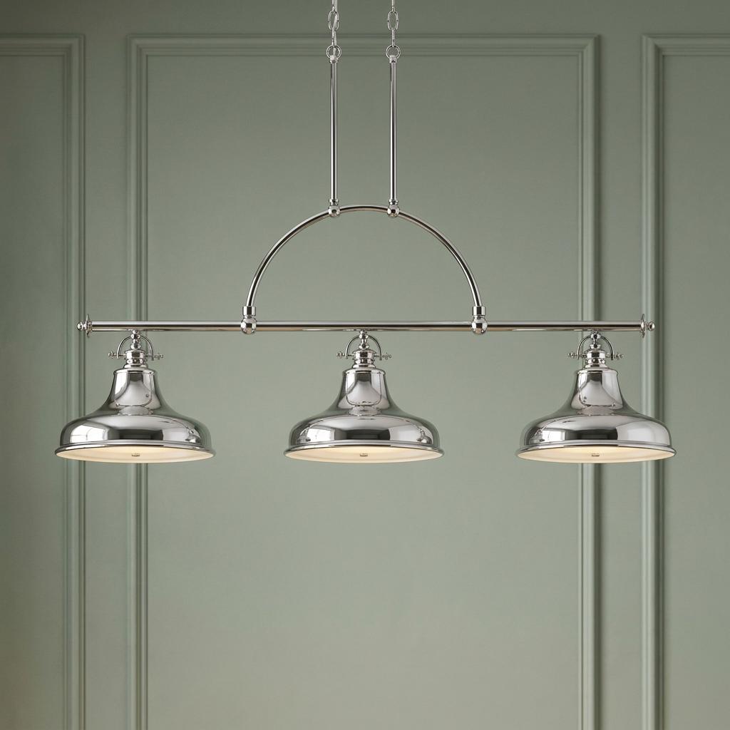 Three-light silver island chandelier with bell-shaped metal shades against a pale green paneled wall.