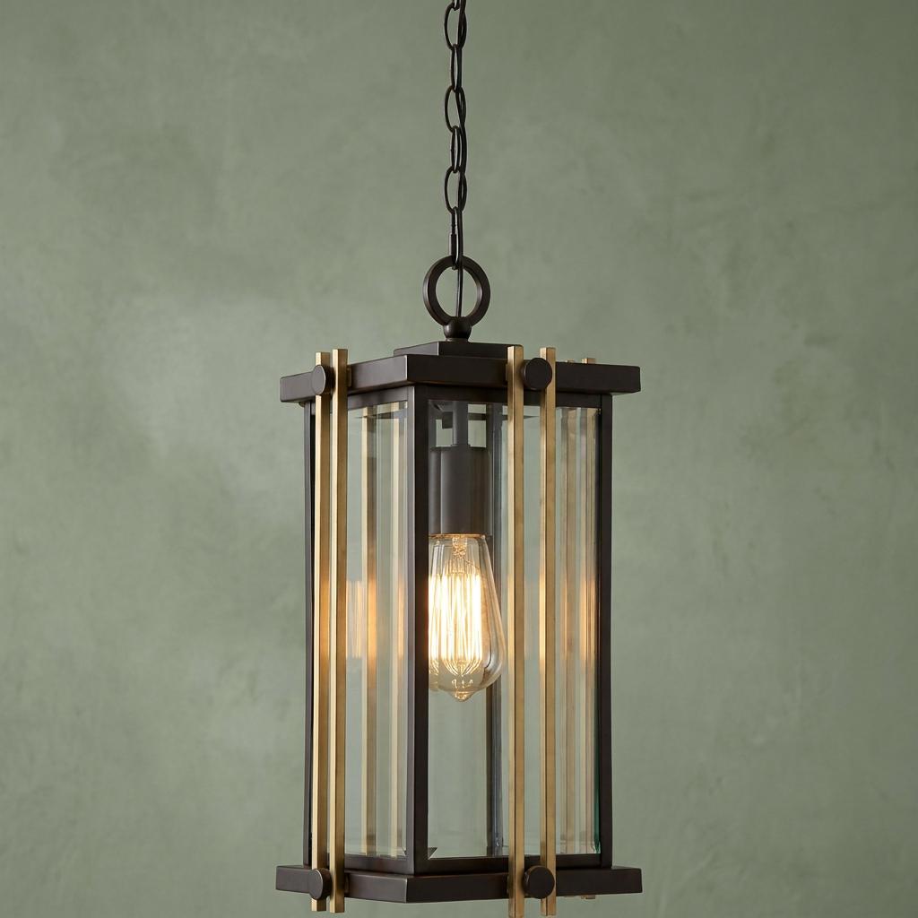 Outdoor lantern pendant with bronze frame, gold vertical bars, and Edison bulb hanging against a sage green wall.