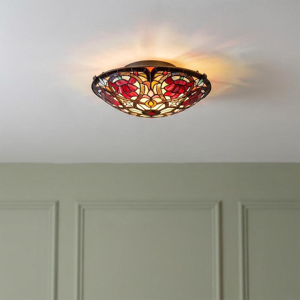 Ornate red and yellow stained glass Tiffany flush mount ceiling light glowing against a white ceiling.