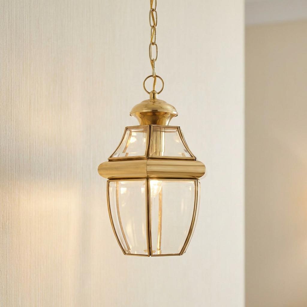 Polished brass chain lantern with clear glass panes hanging against a neutral textured wall.