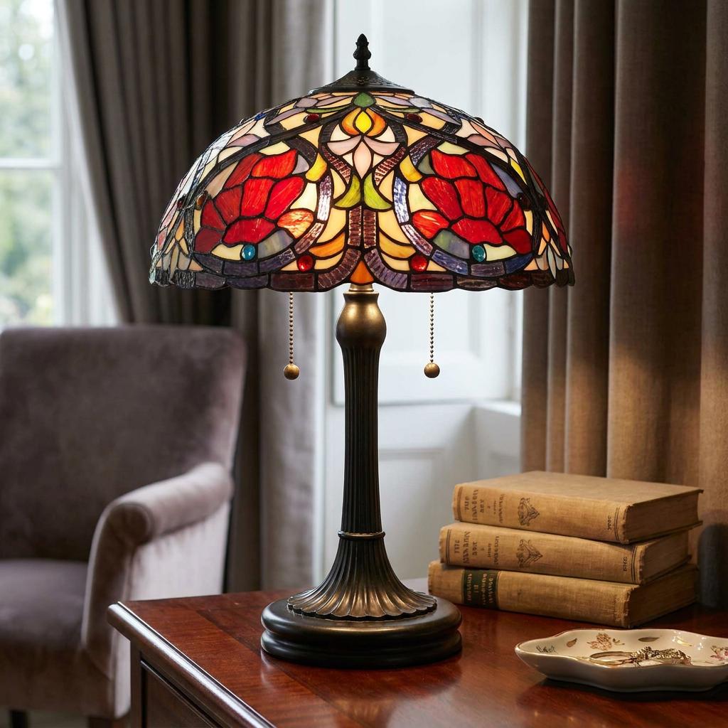 Tiffany-style table lamp with a colorful floral stained glass shade sitting on a wooden table beside old books.