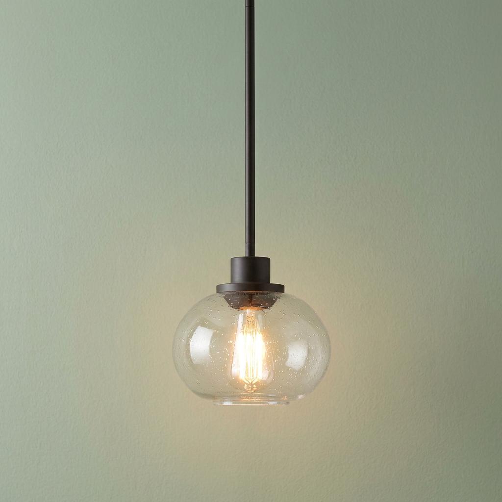 A bronze ceiling pendant with a seeded glass globe and a glowing vintage bulb against a soft green wall.