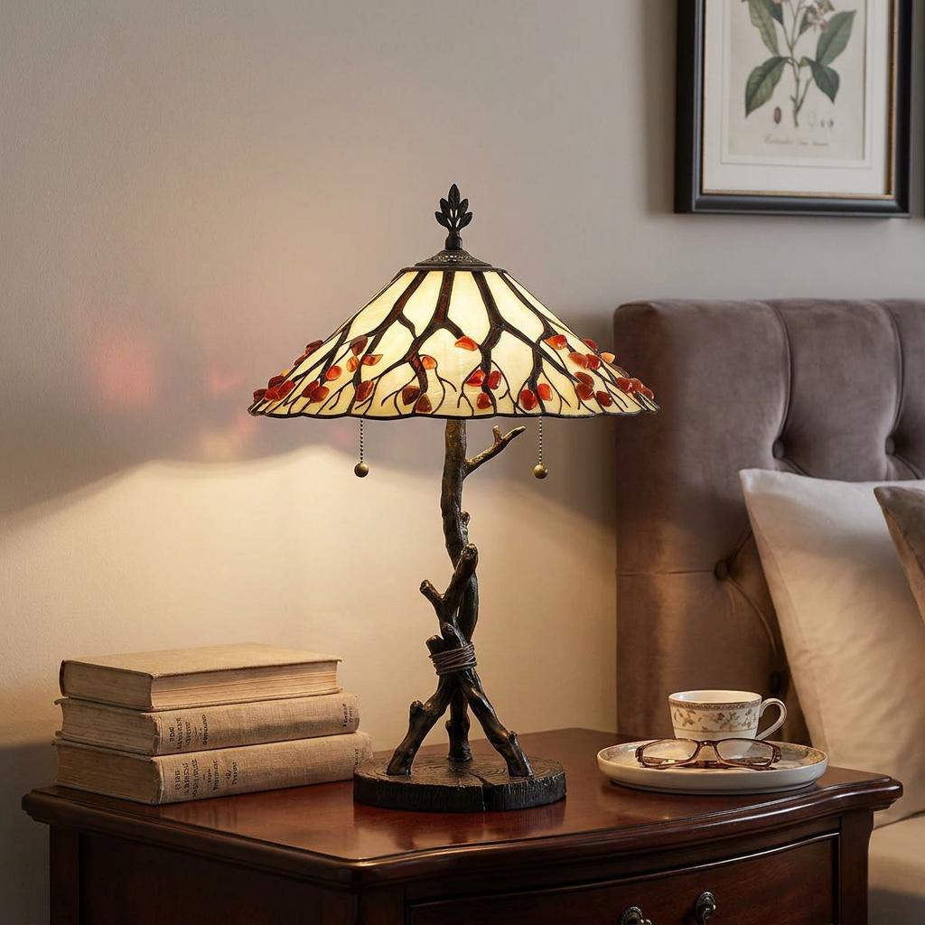 Tiffany-style table lamp with a branch-themed base and berry-accented shade on a nightstand with books.