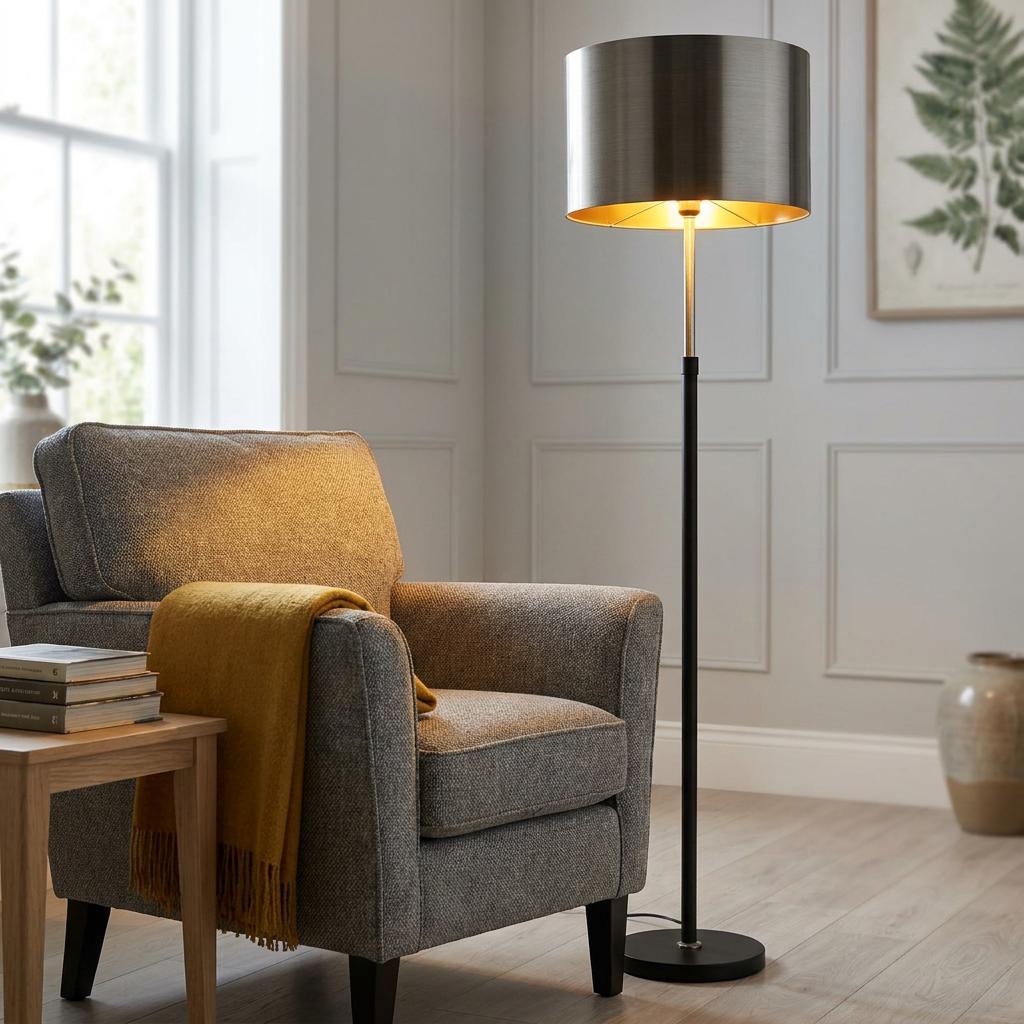 Rachel Black & Chrome Floor Lamp with a metallic shade casting light on a grey armchair in a modern living room.