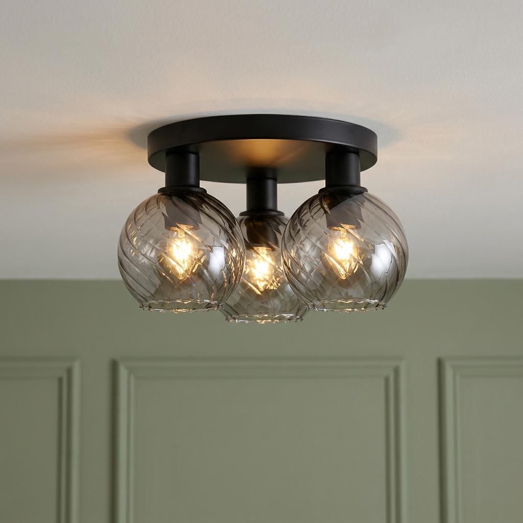 Three-light flush mount ceiling fixture with black metal base and smokey swirl glass globes against a green wall.