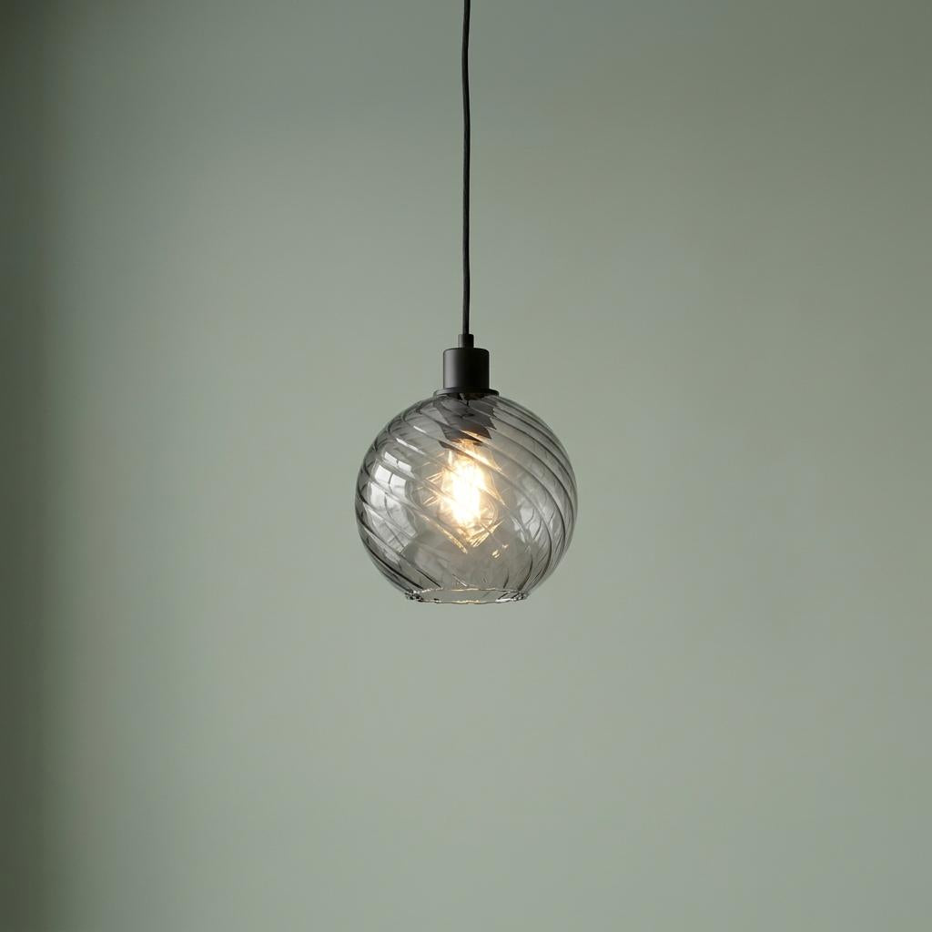 Smoke-tinted swirled glass globe pendant light with a black fixture, glowing against a pale green wall.