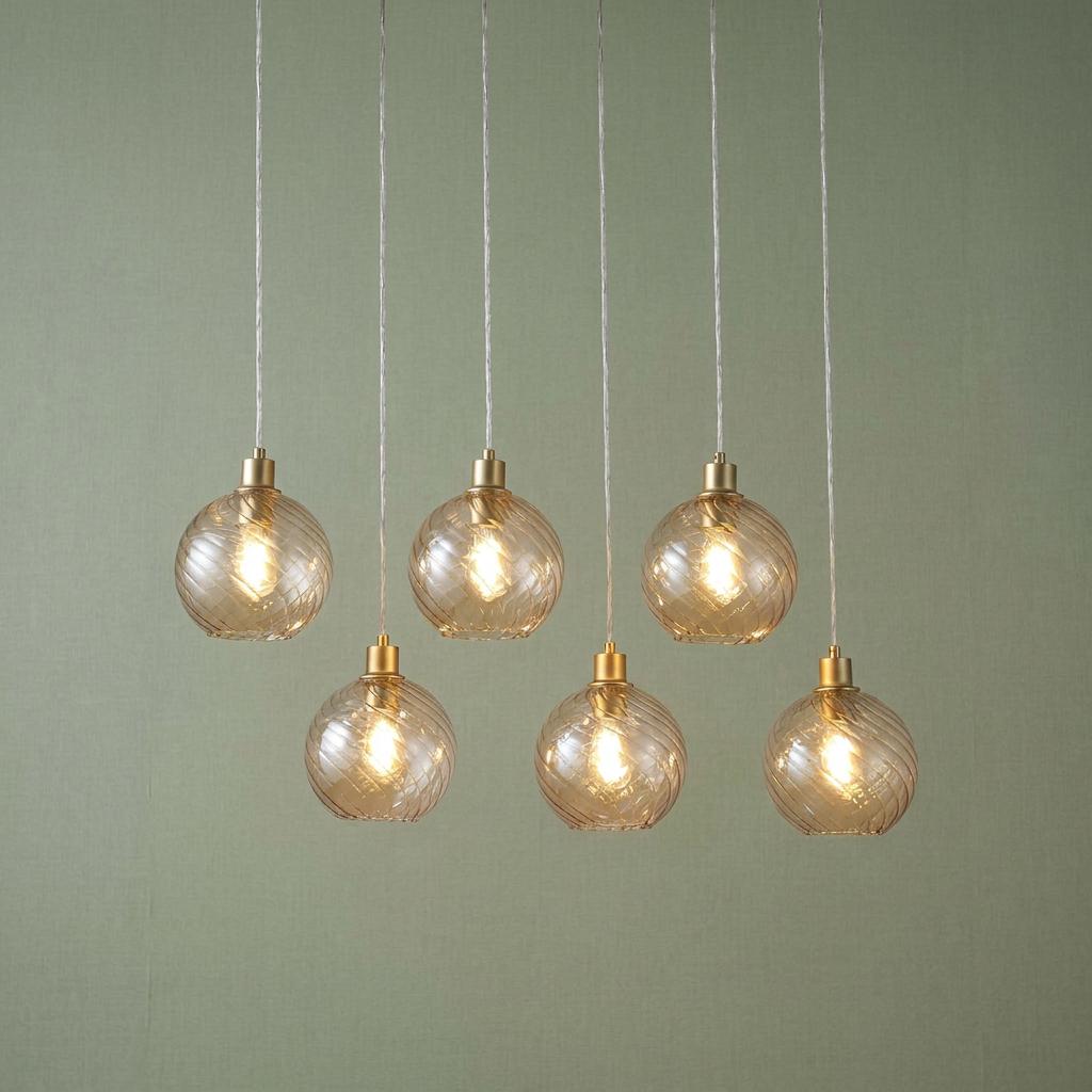 Six staggered pendant lights with champagne ribbed glass globes and gold fittings against a sage green background.
