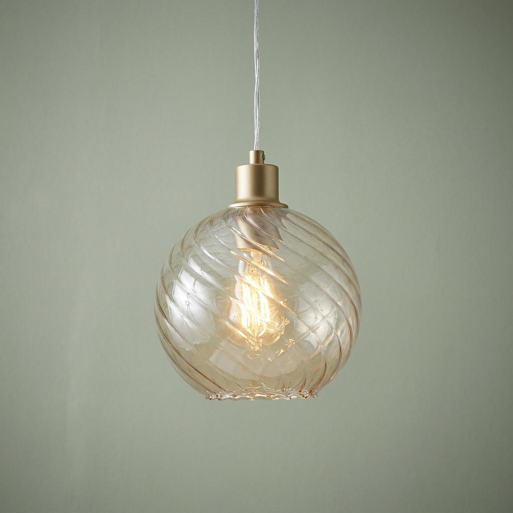 A gold-finished pendant light with a champagne ribbed glass globe shade against a pale green wall.