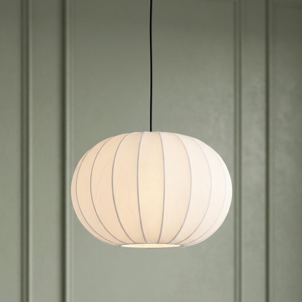 A glowing white ribbed fabric pendant light hangs against a sage green paneled wall.