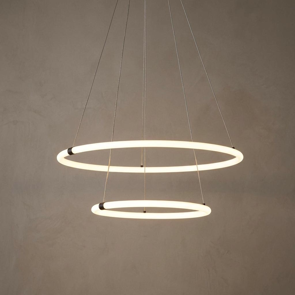 Two tiered glowing opal LED ring pendants suspended by thin cables against a textured neutral wall.