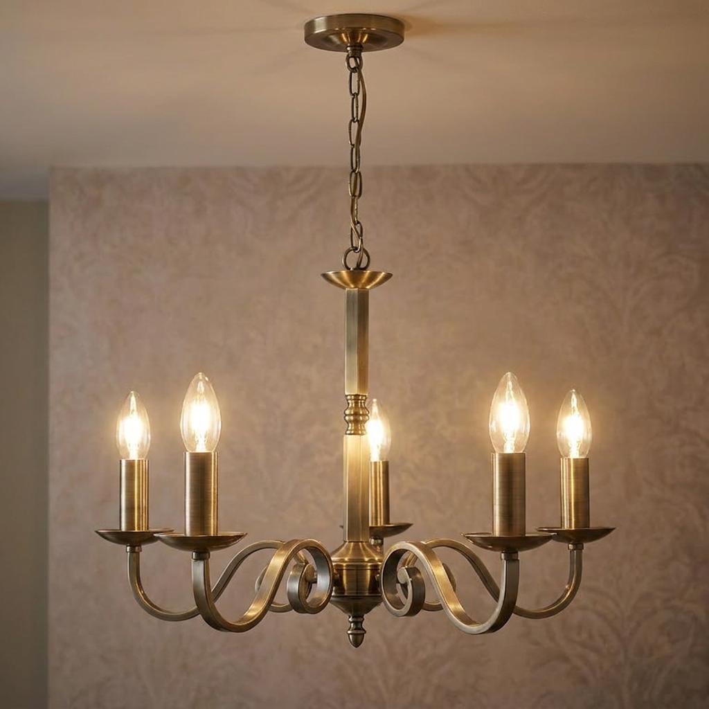 Antique brass five-light chandelier with scroll arms and lit candle bulbs against a patterned background.