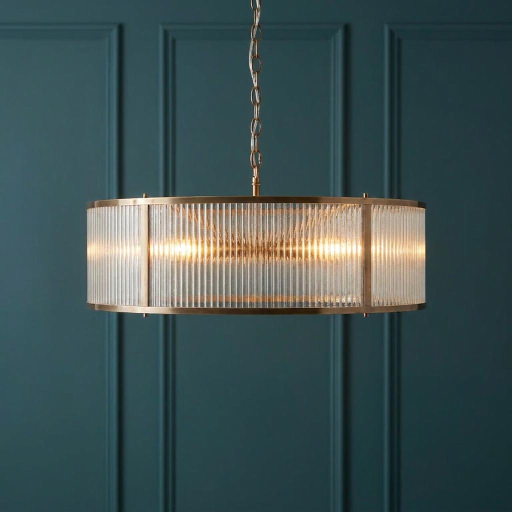 Ridgeton 8-light antique brass pendant with ribbed glass shade against a dark teal paneled wall.