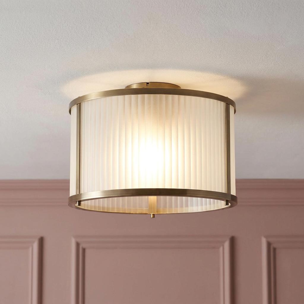 Ridgeton antique brass flush ceiling light with frosted fluted glass shade against a pink paneled wall.