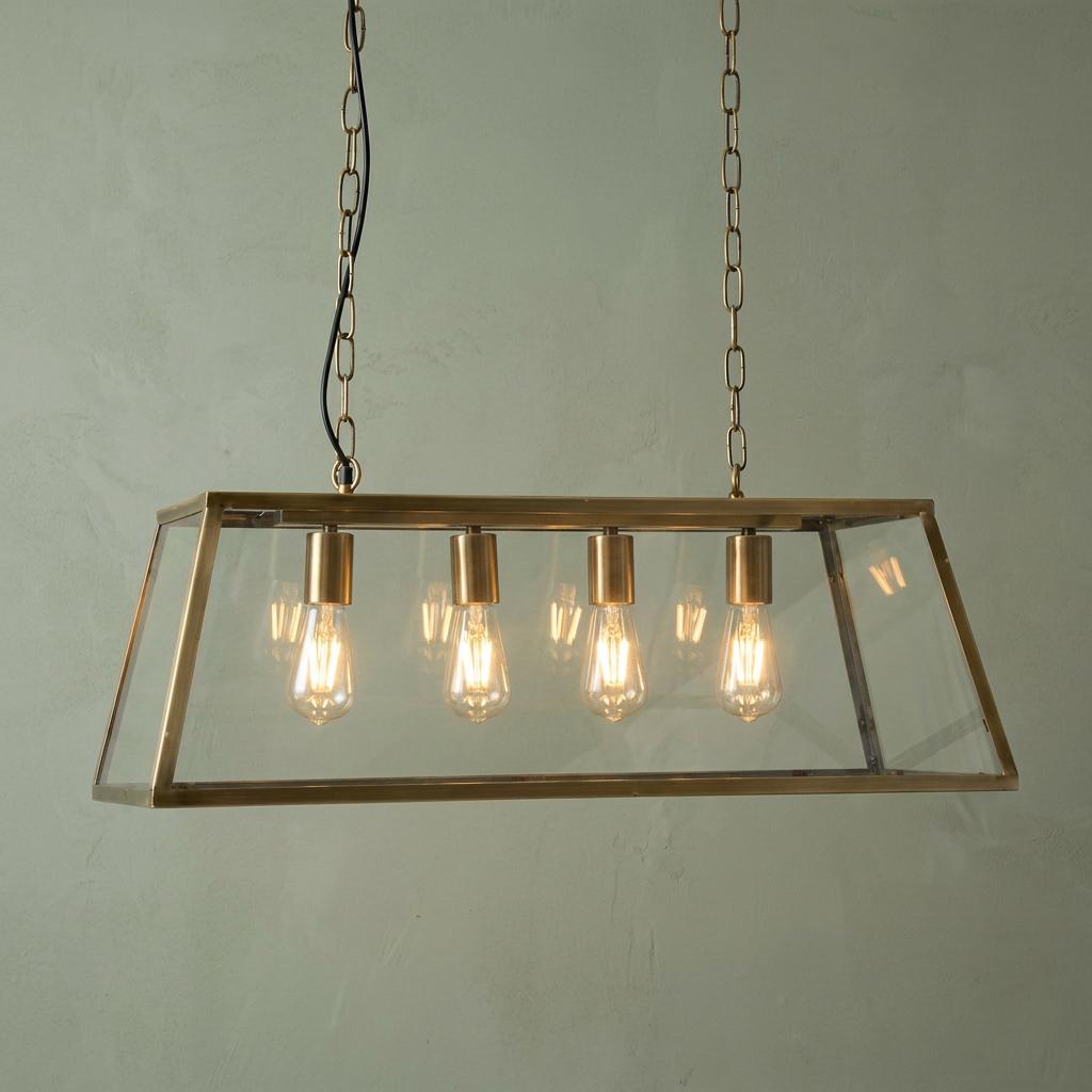 Riga 4-light antique brass pendant with clear glass panels and glowing filament bulbs against a green wall.