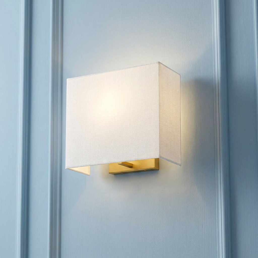 Rectangular wall light with a white fabric shade and aged brass base glowing against a light blue paneled wall.