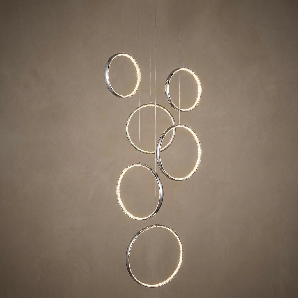 Modern chrome pendant light with six illuminated circular rings suspended at varying heights against a textured wall.