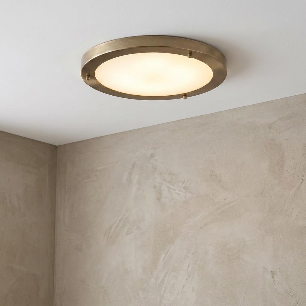 Large circular flush ceiling light with an antique brass frame and glowing frosted glass mounted in a neutral room.