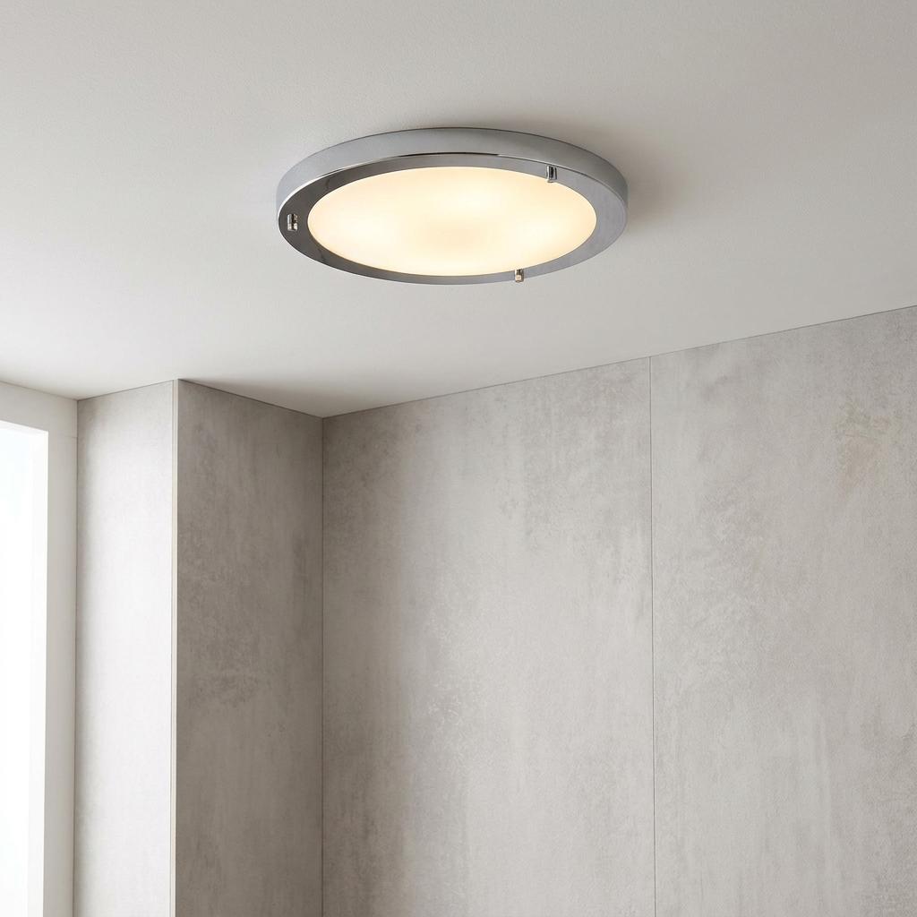 Round chrome-rimmed flush ceiling light with a warm glow mounted in a modern grey-tiled bathroom.