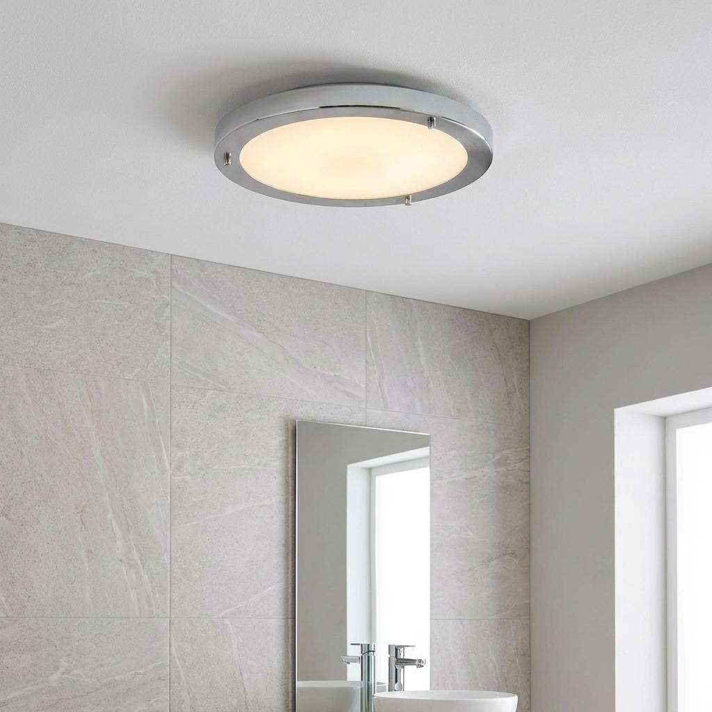 Rondo chrome flush ceiling light with warm illumination in a tiled modern bathroom setting.