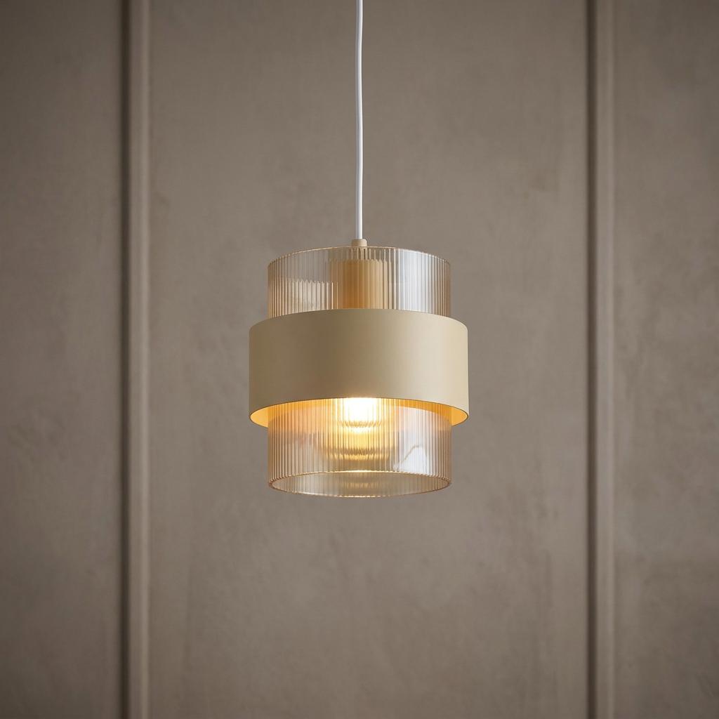 Sand metal pendant light with a ribbed glass shade glowing warmly against a neutral paneled wall.