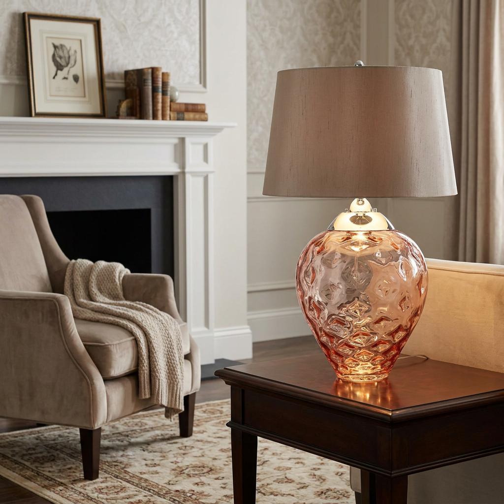 Samara salmon pink glass table lamp with a taupe shade sitting on a dark wood end table in a living room setting.
