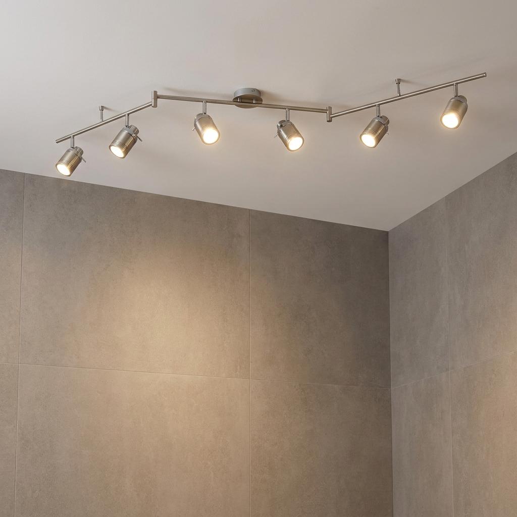 Six silver adjustable spotlights on a split-bar ceiling track illuminate a grey-tiled bathroom wall.