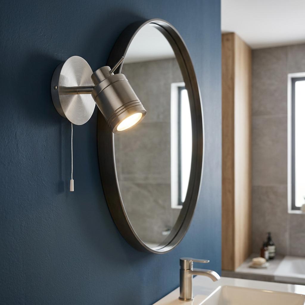 Samson silver adjustable wall spotlight with pull switch, mounted next to a round mirror on a dark blue wall.