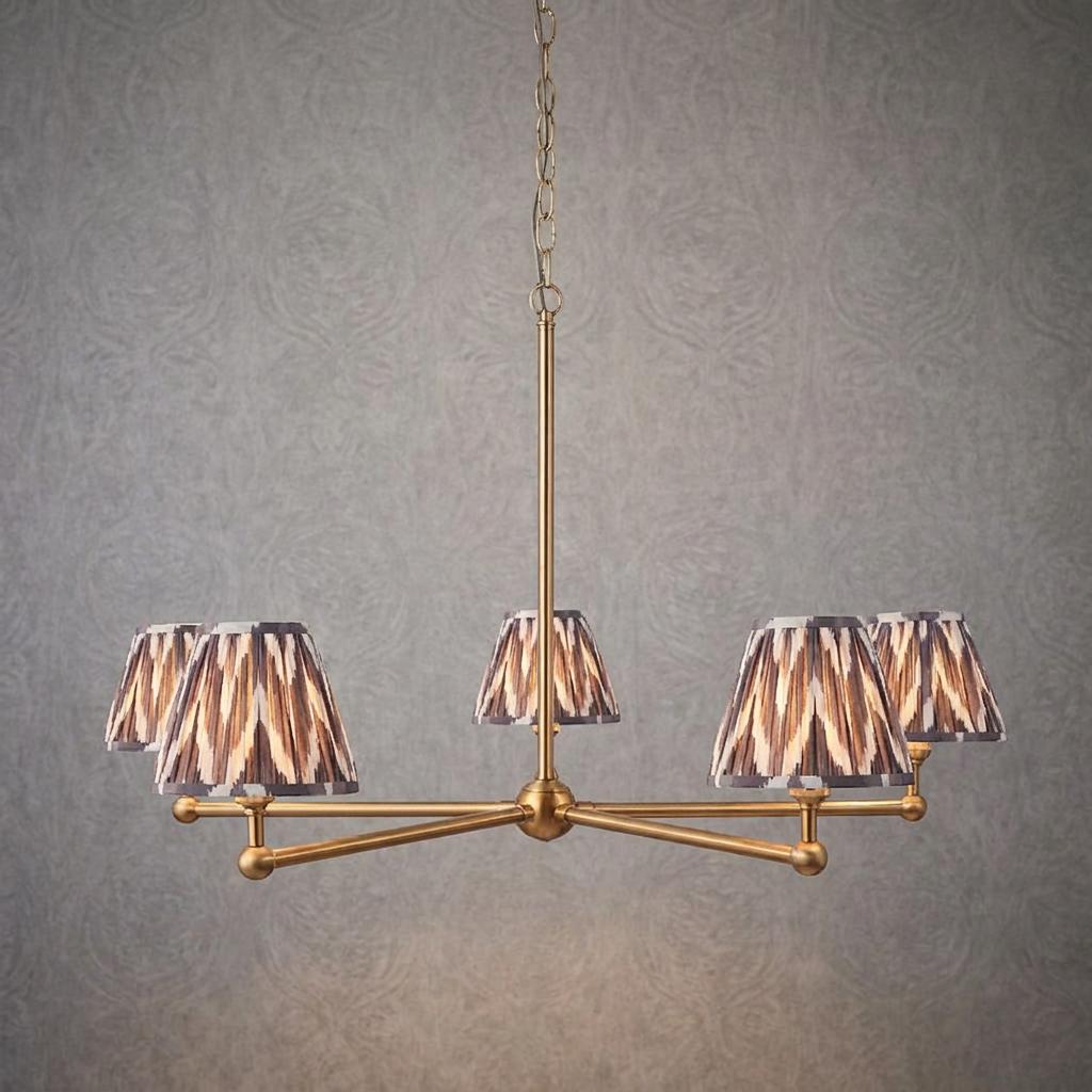 Santiago Brass 5 light pendant ceiling light with grey zigzag ikat shades hanging against a patterned grey wall.