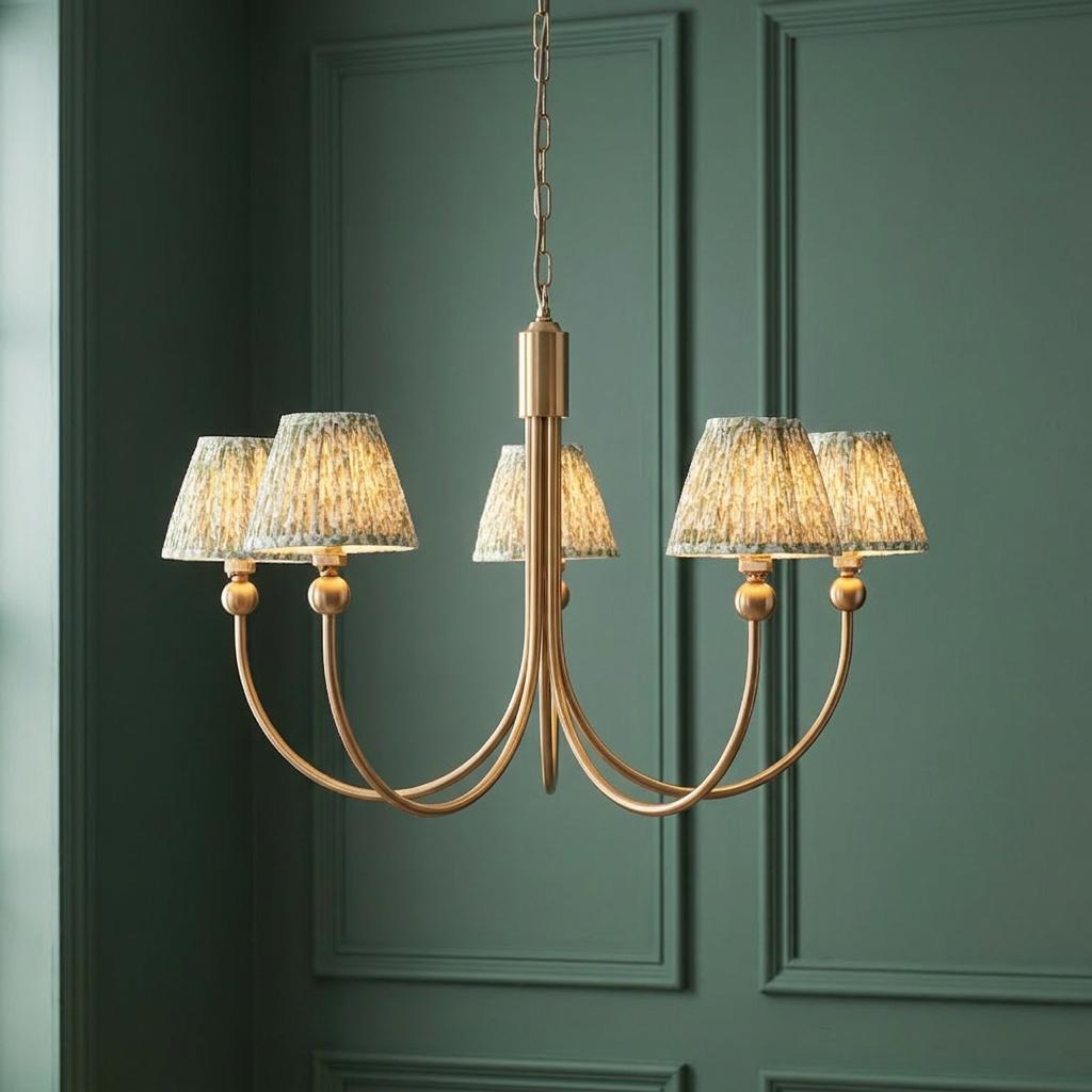 Five-arm brass chandelier with green leaf-patterned shades hanging against a dark green paneled wall.