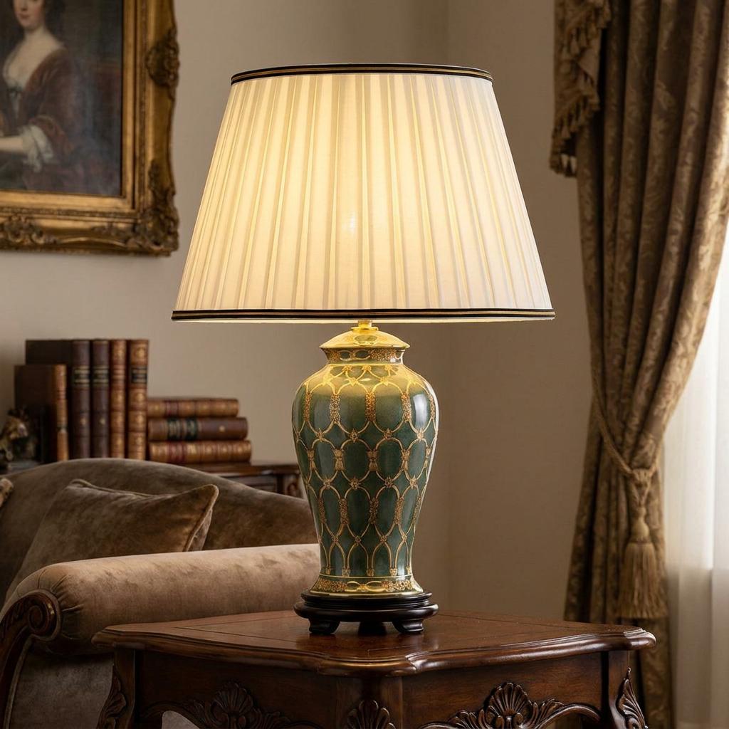 Illuminated green and gold ceramic lamp with a pleated ivory shade on a wooden side table in a traditional room.