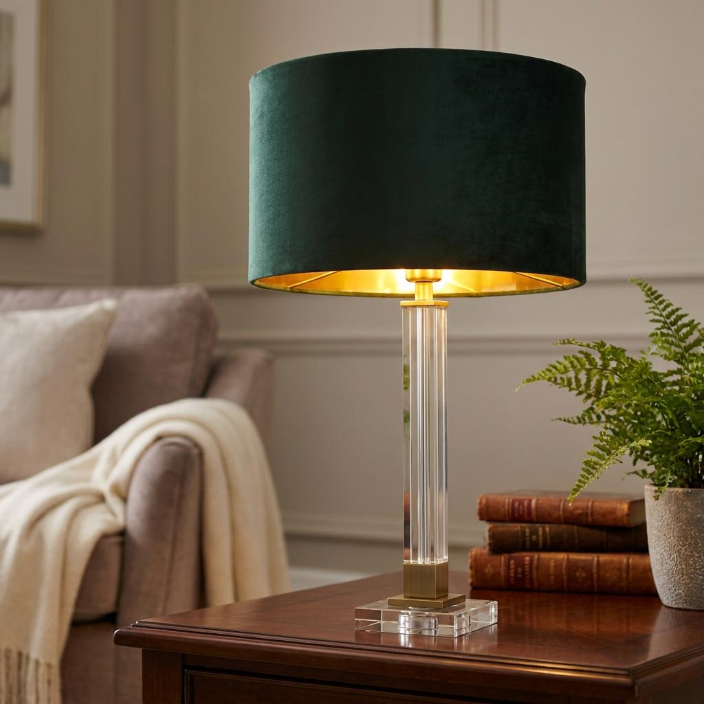 Crystal table lamp with a green velvet shade and brass accents on a wooden table in a warm interior.