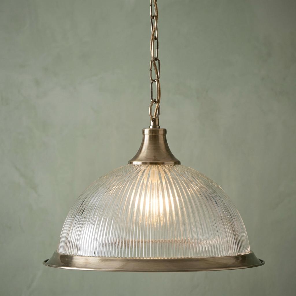 A Searchlight American Diner pendant light with a ribbed glass shade and brass trim against a green wall.