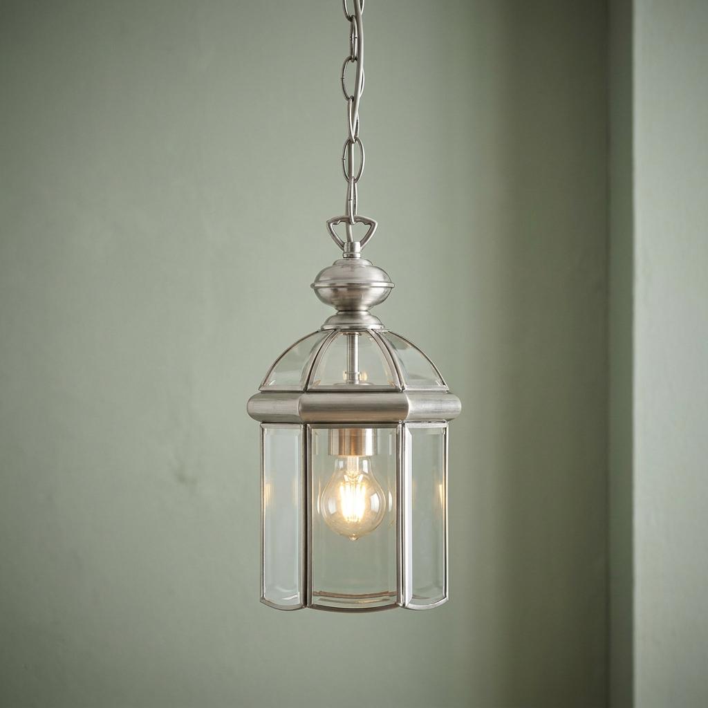 Domed glass lantern pendant light with a metal frame hanging from a chain against a pale green wall.