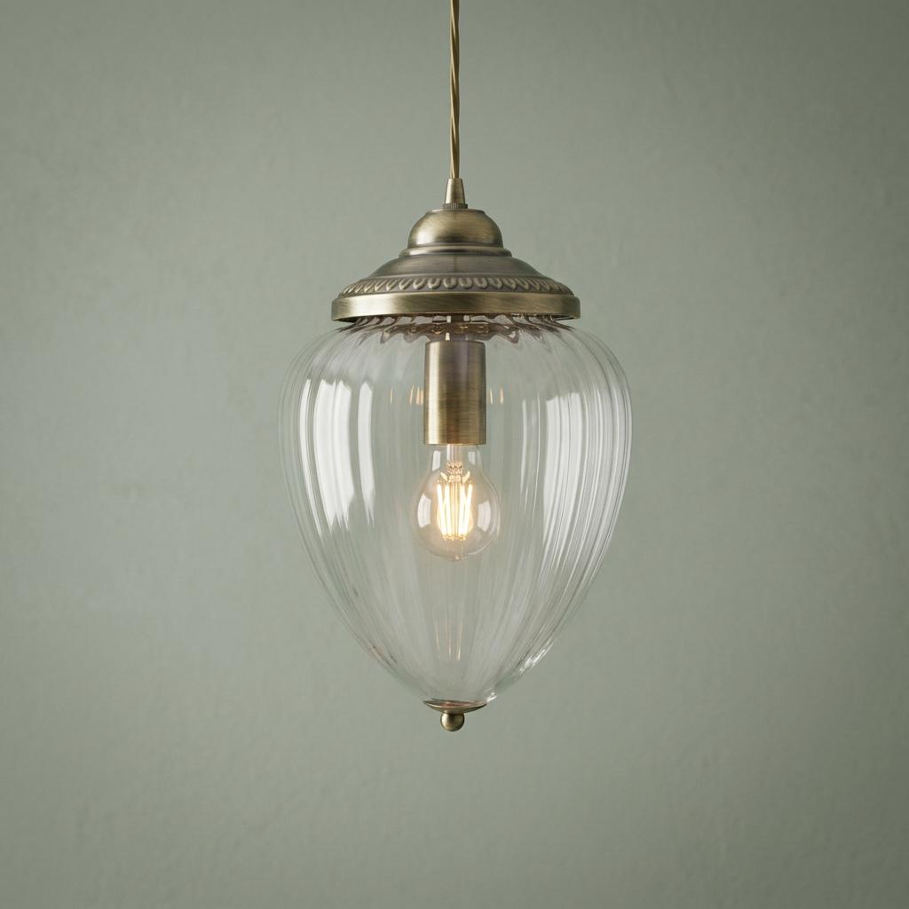 Antique brass ceiling light with a clear ribbed glass acorn shade and a glowing bulb against a green wall.