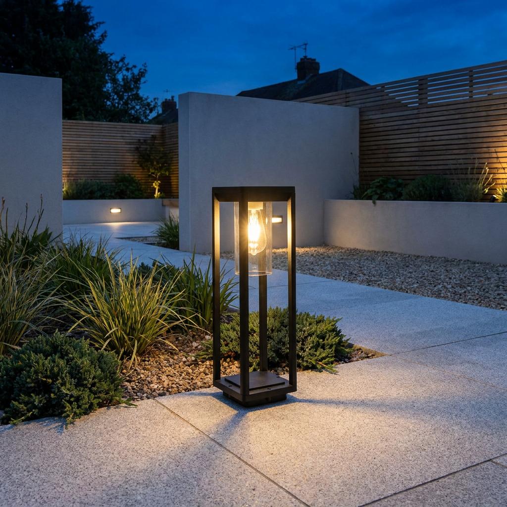 Modern black rectangular outdoor bollard light illuminating a stone pathway in a landscaped garden at twilight.