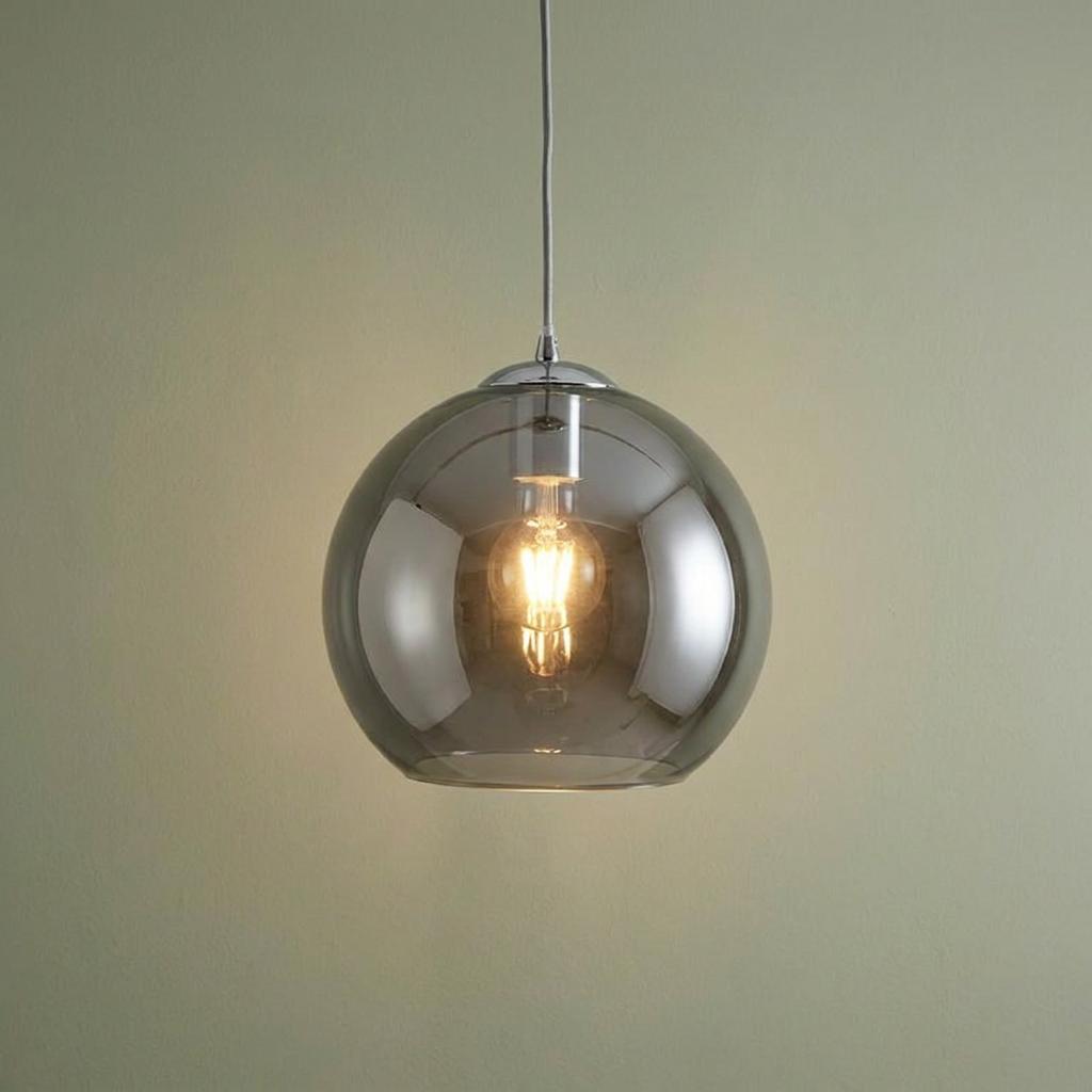Illuminated smoked glass globe pendant light with chrome accents against a neutral wall.