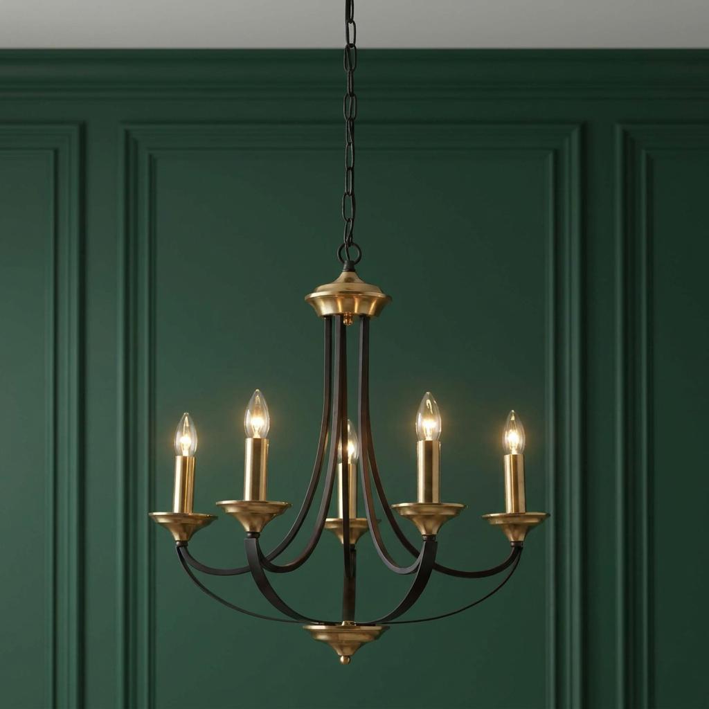 Five-light bronze and brass chandelier with lit candle bulbs against a dark green paneled wall.